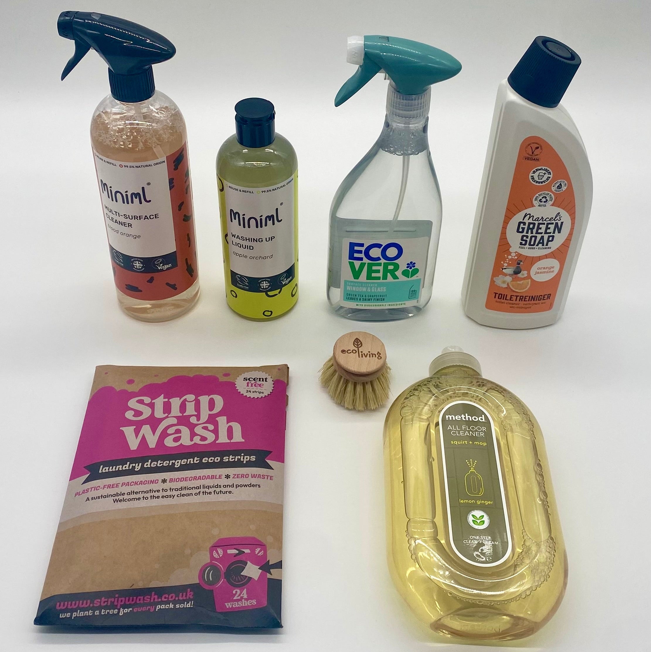 Collection of non toxic eco cleaning products including bottles, a packet, and a brush on a white background